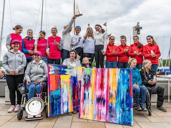 18 Frauen stehen auf dem Pier und freuen sich über ihren Sieg.