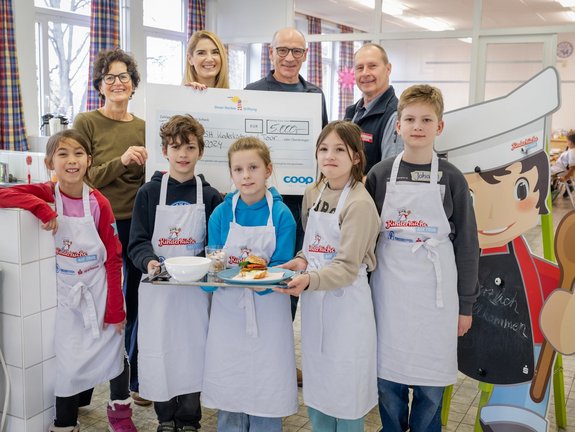 Im Vordergrund stehen fünf Kinder. Hinter diesen stehen zwei Frauen und zwei Männer und halten einen Spendencheck in der Hand.